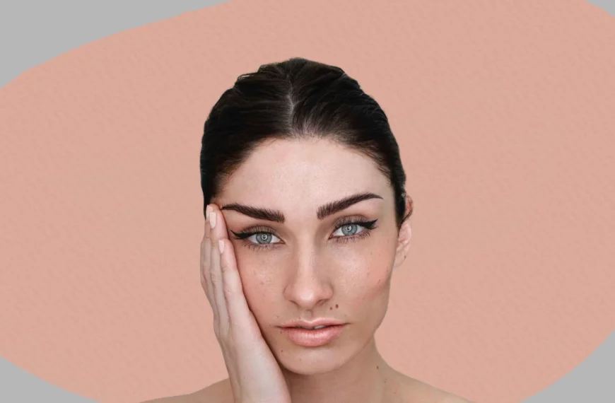 headshot of woman looking into camera, hand on face, eyebrows define and shaped