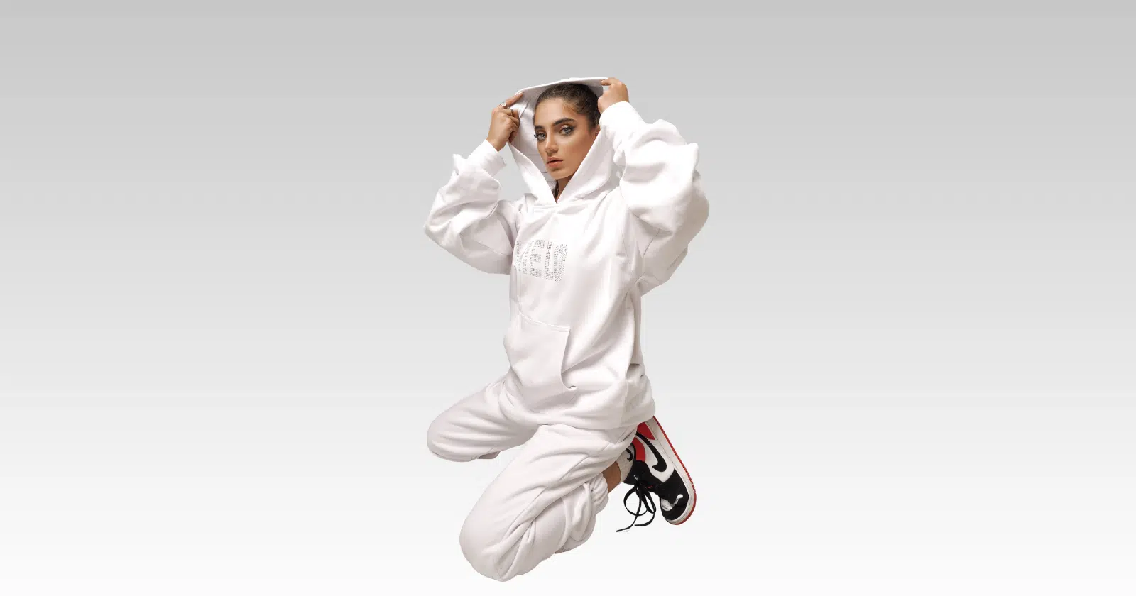 woman sitting on knees, dressed in all white sweatshirt and sweatpants