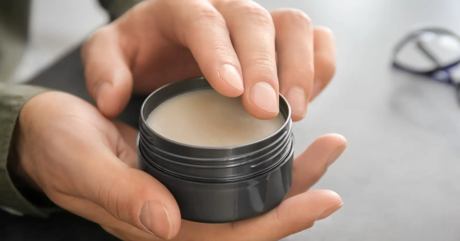 closeup of person's hands holding tub of hair wax or pomade