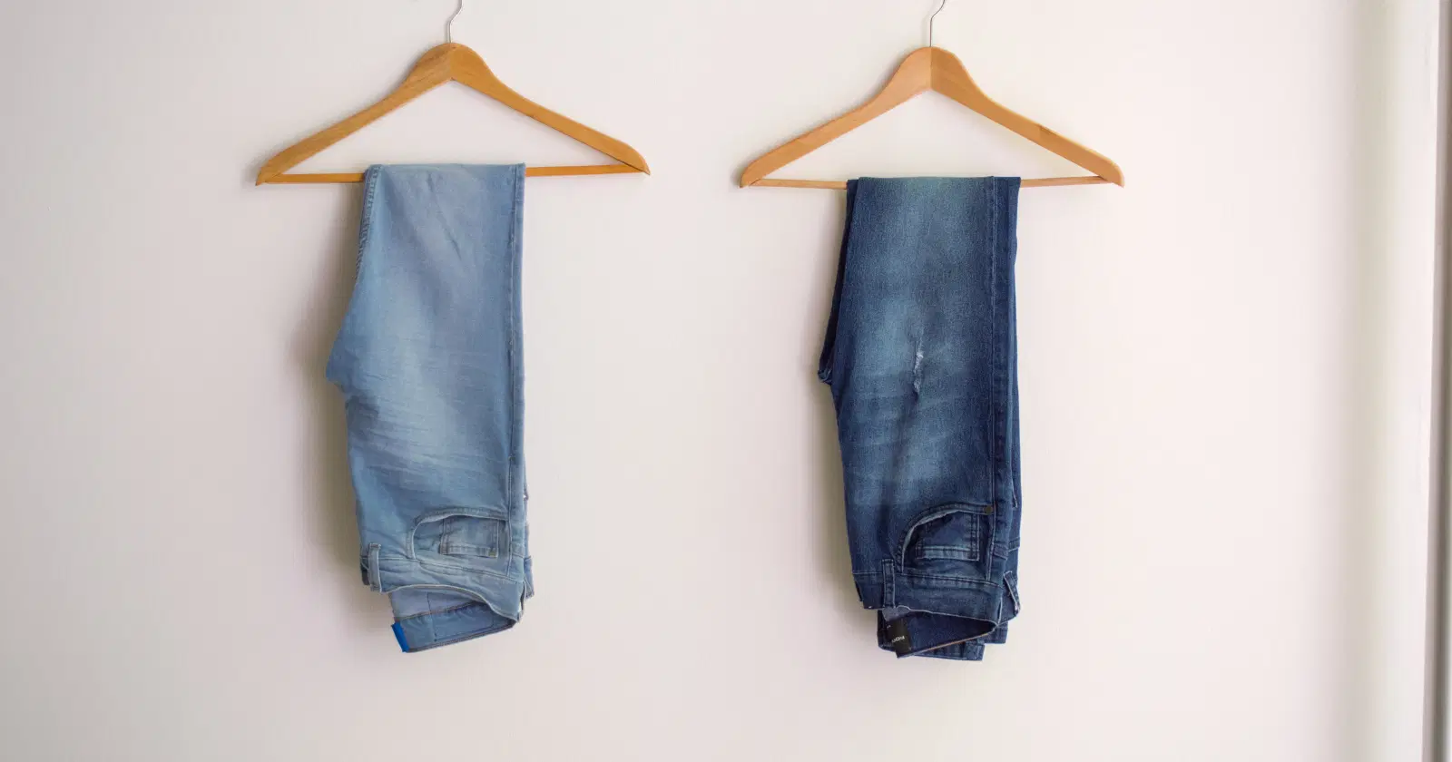 two pairs of jeans, one light one dark, hanging next to each on brown hangers