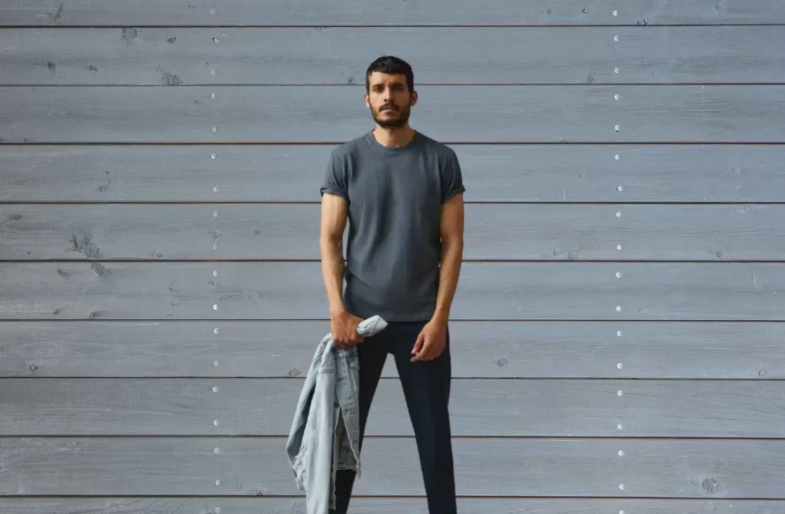 man looking at camera wearing gray shirt, dark pants, holding jean jacket from American Giant