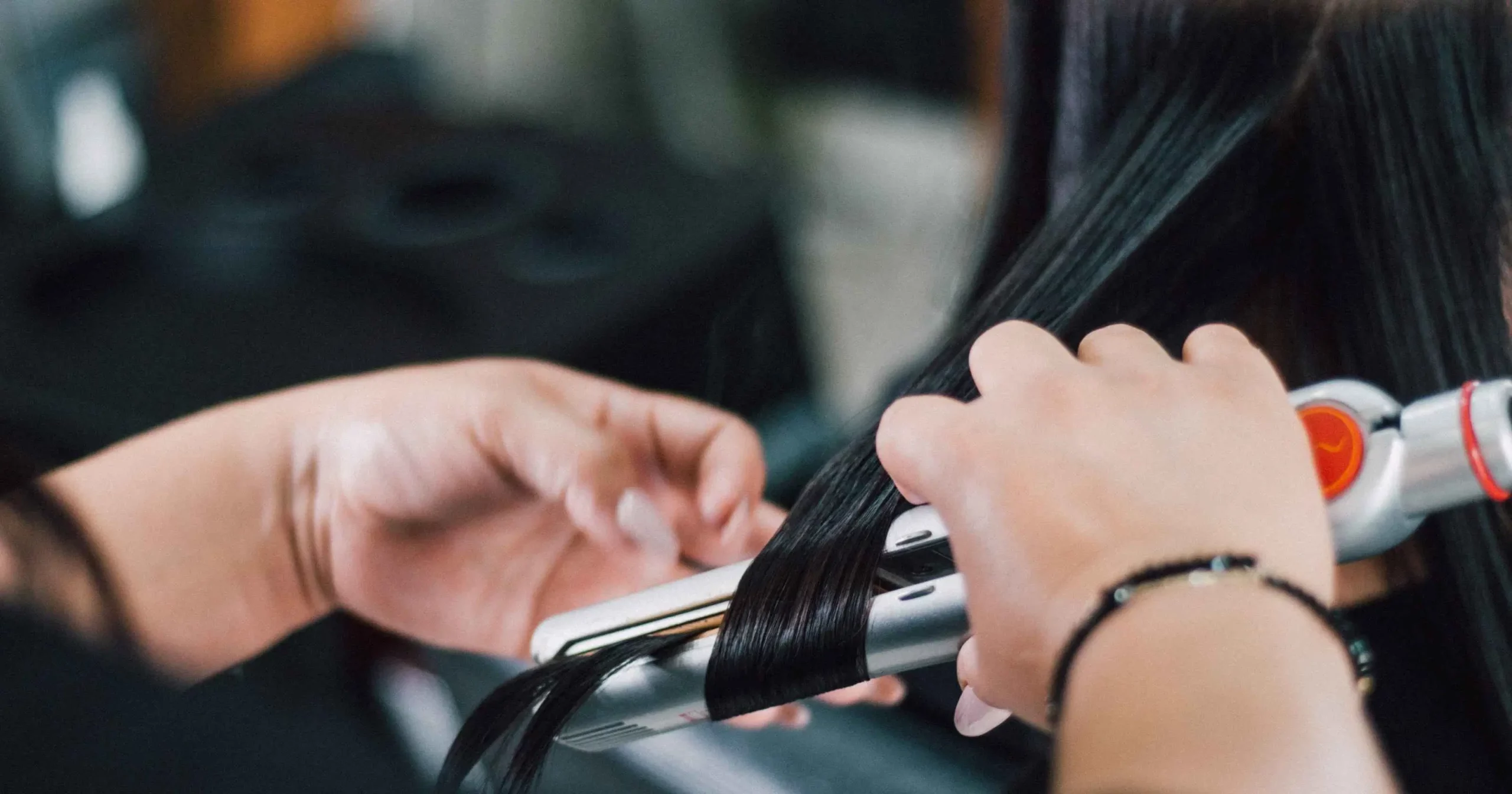 close up of hands using a hair straightener on long dark hair