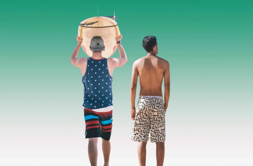 two men turned around, one wearing striped board shorts and blue tank with surfboard on head, the other wearing patterned swim trunks