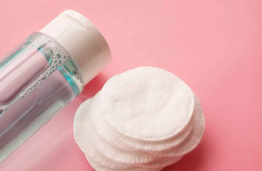 micellar water or toner in clear bottle lying next to round cotton pads