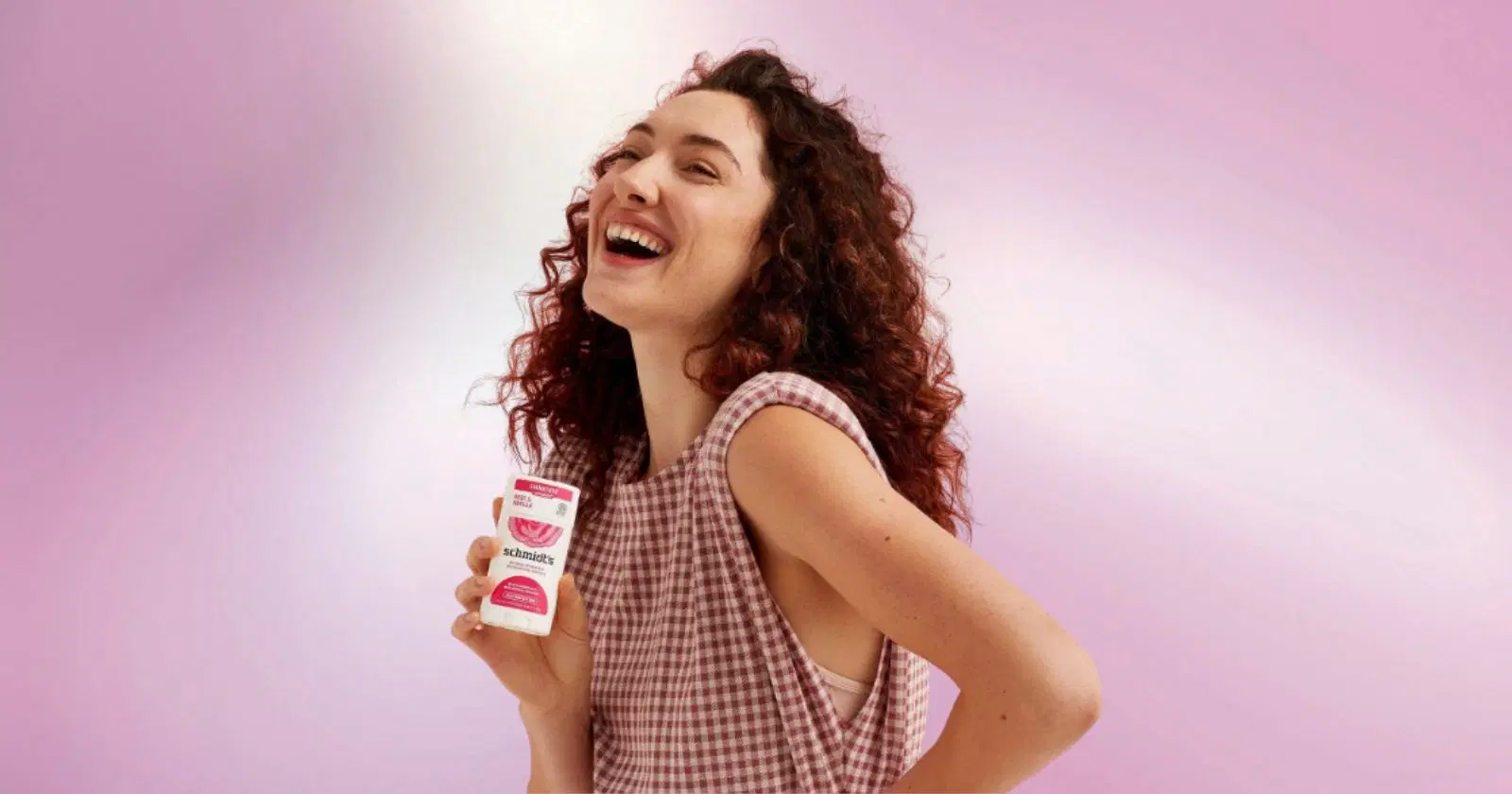 woman with curly hair looking off camera, smiling, holding Schmidt's natural deodorant