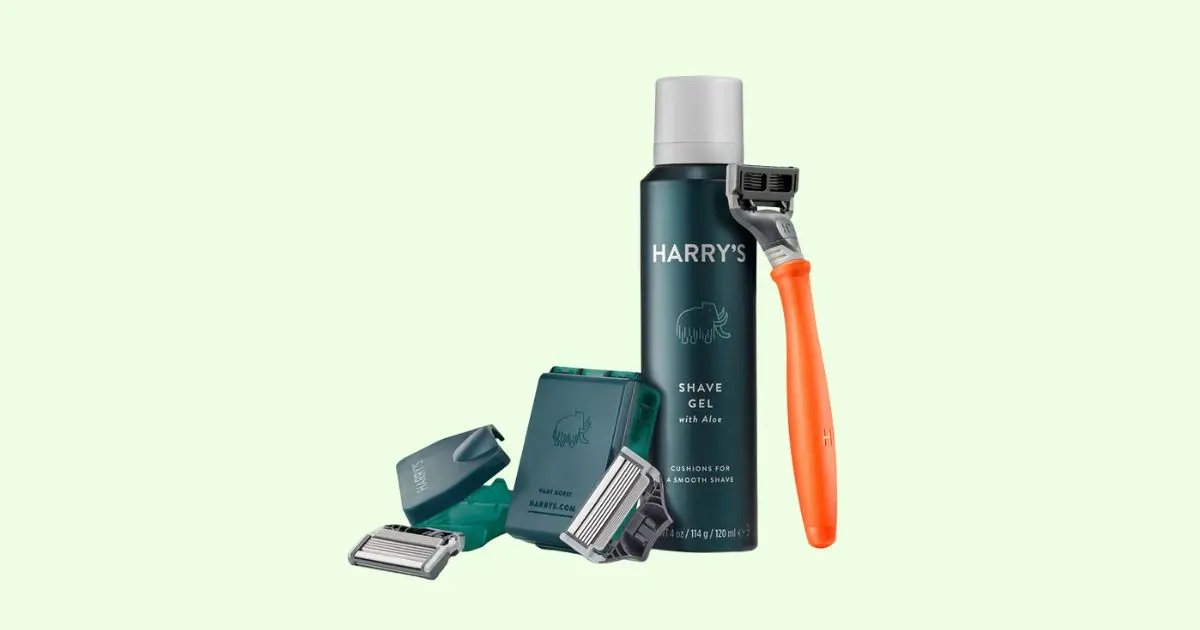 harry's razor bundle that showcases the brand's Truman razor with orange colored handle, shave gel, two replacement blades with a holding box, and a razor cover. Photo has a pastel green background.